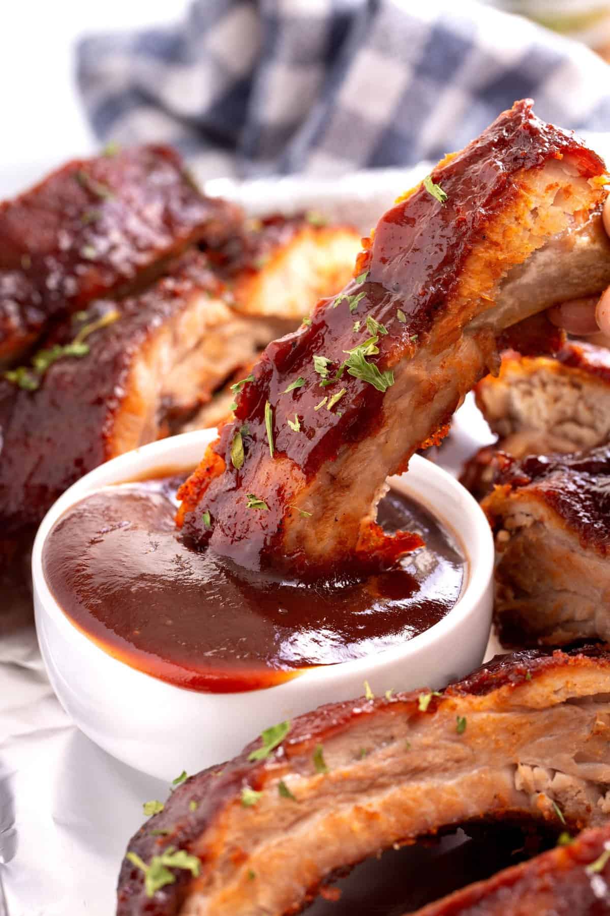 crock pot rib dipping into a bowl of barbecue sauce
