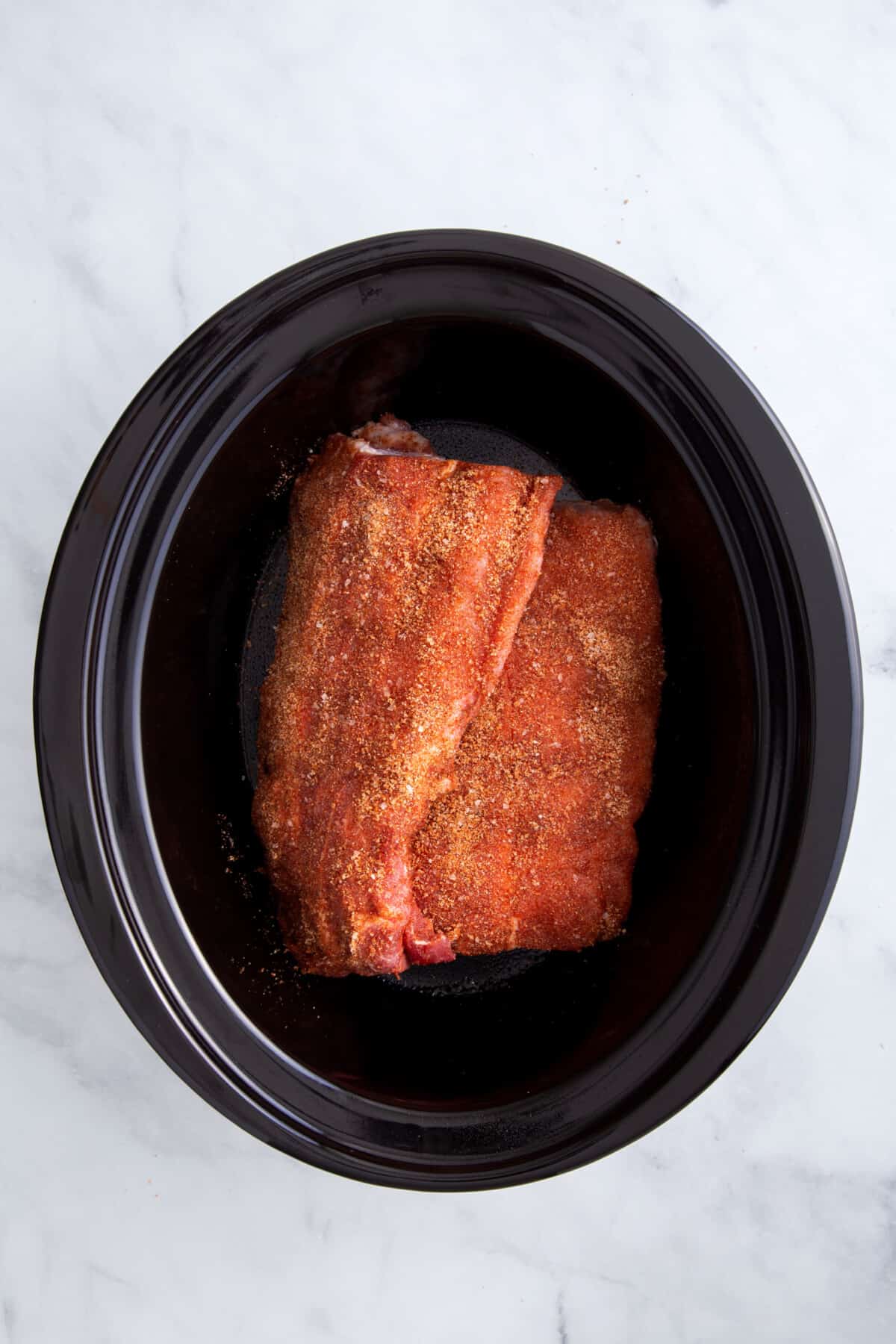 dry rubbed pork ribs sitting in a slow cooker.