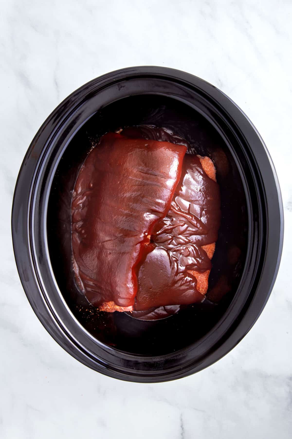 dry rubbed with barbecue sauce pork ribs sitting in a slow cooker.