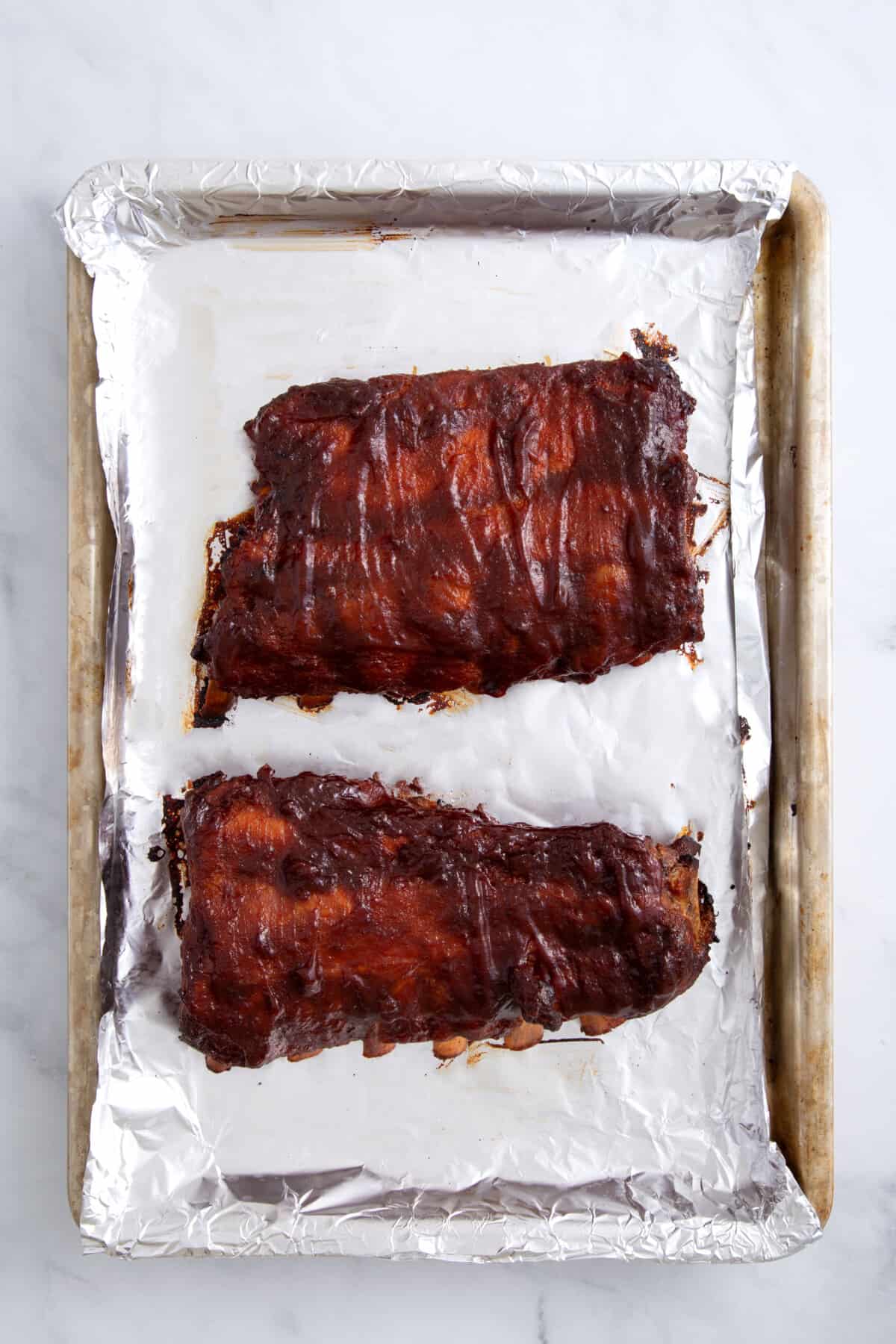 two crock pot ribs sitting on a foil-lined baking sheet.