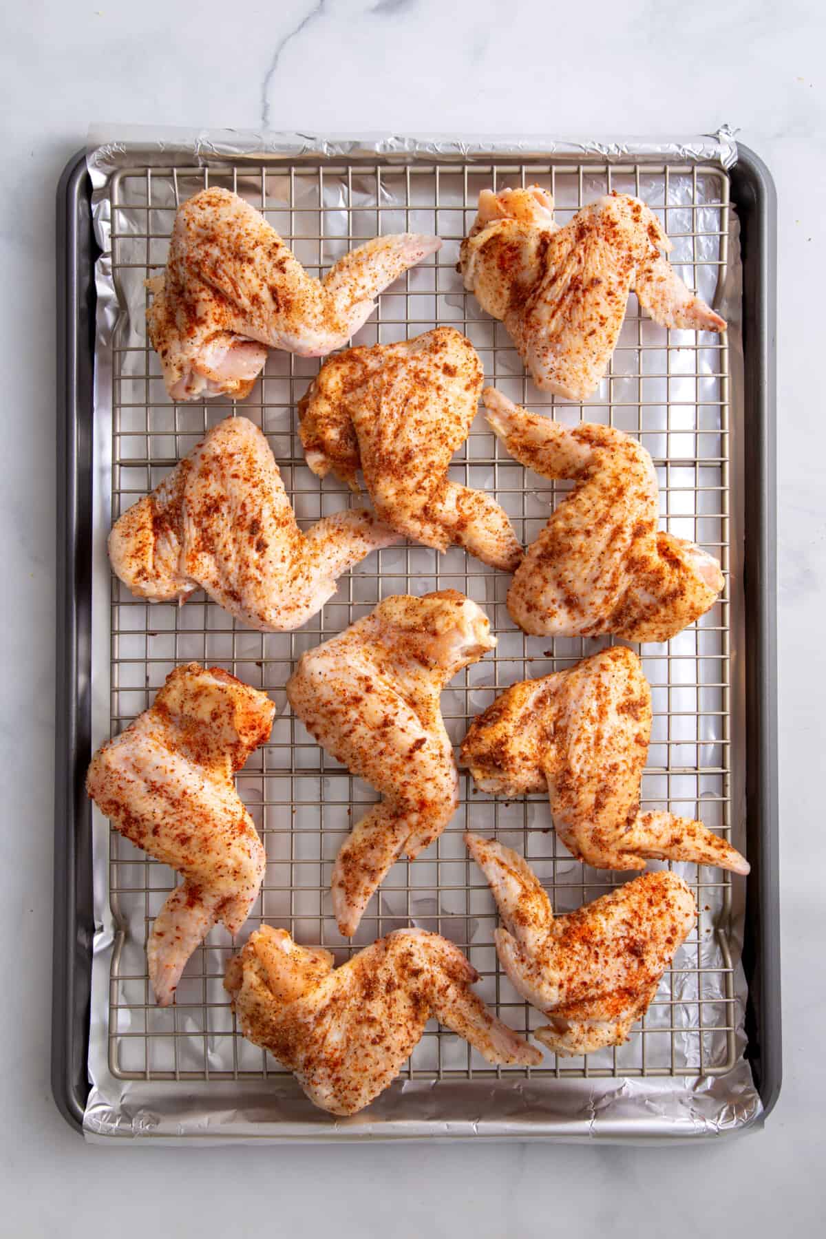 seasoned uncooked chicken wings sitting on a wire rack and foil-lined baking sheet