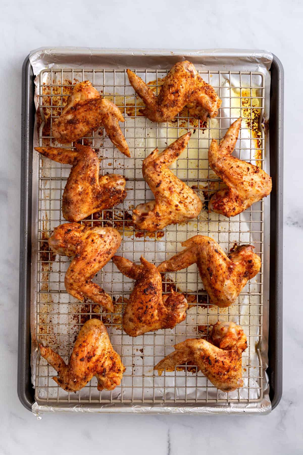 seasoned uncooked chicken wings sitting on a wire rack and foil-lined baking sheet