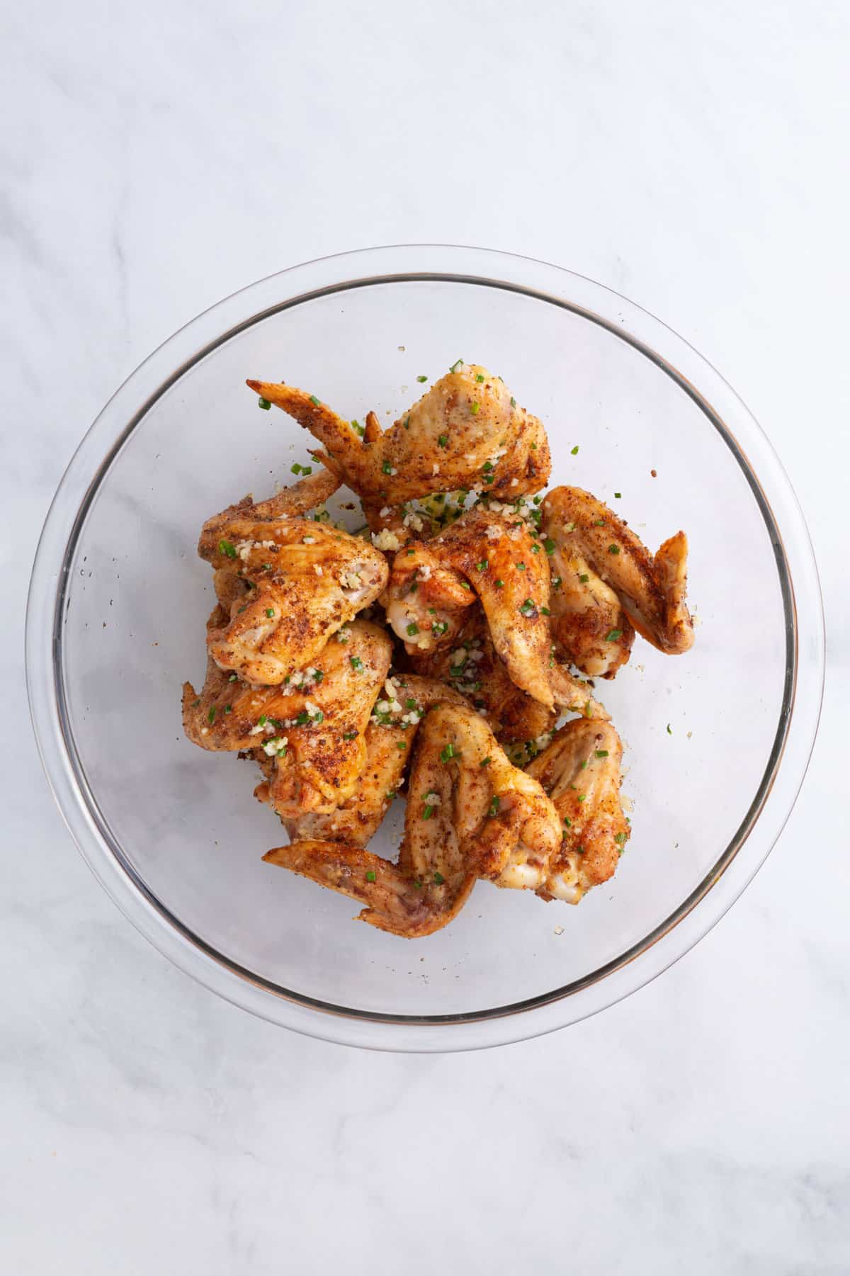 seasoned chicken wings tossed with garlic butter sitting in a large glass bowl