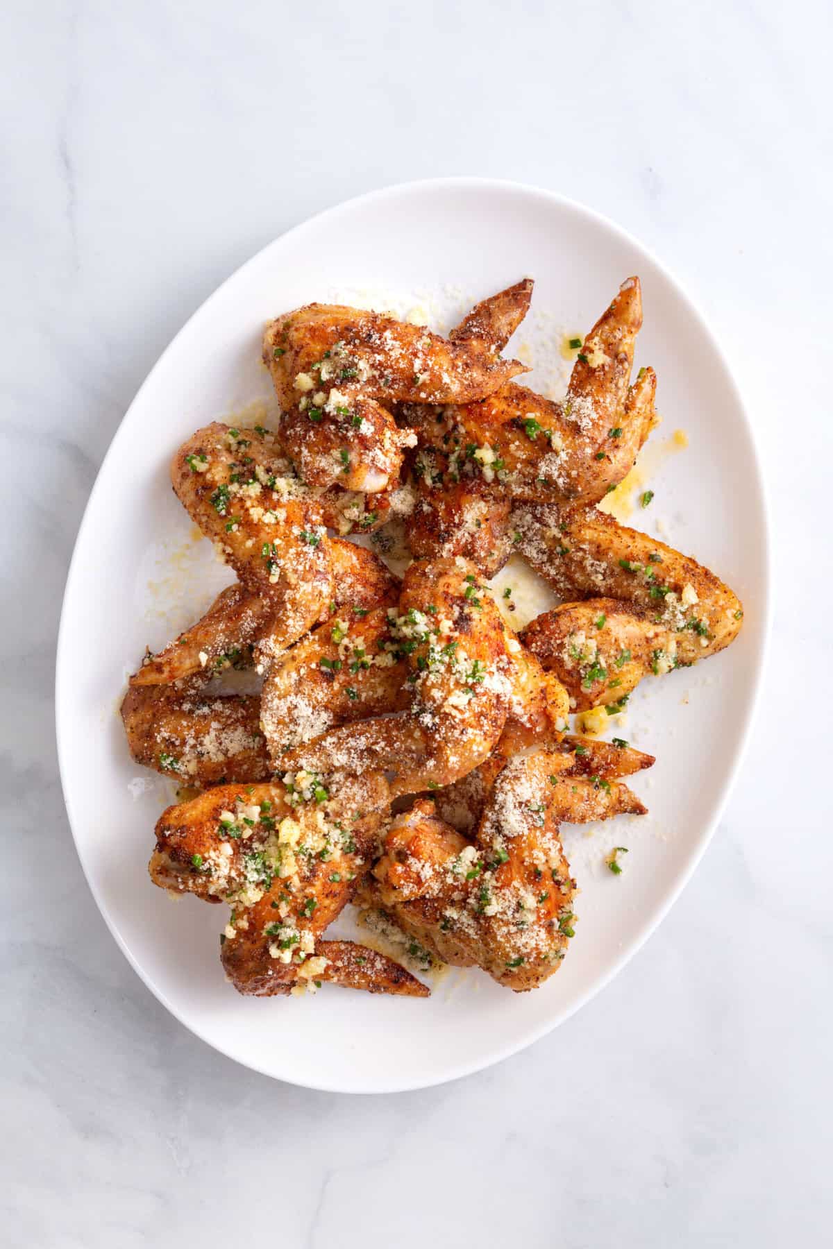 top down image of garlic parmesan chicken wings sitting on a large oval plate