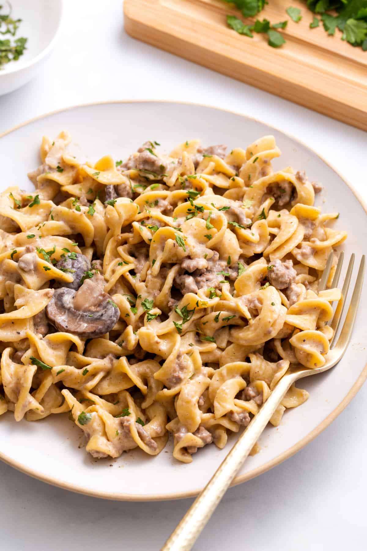 serving of ground beef stroganoff sitting on a round plate with a gold fork