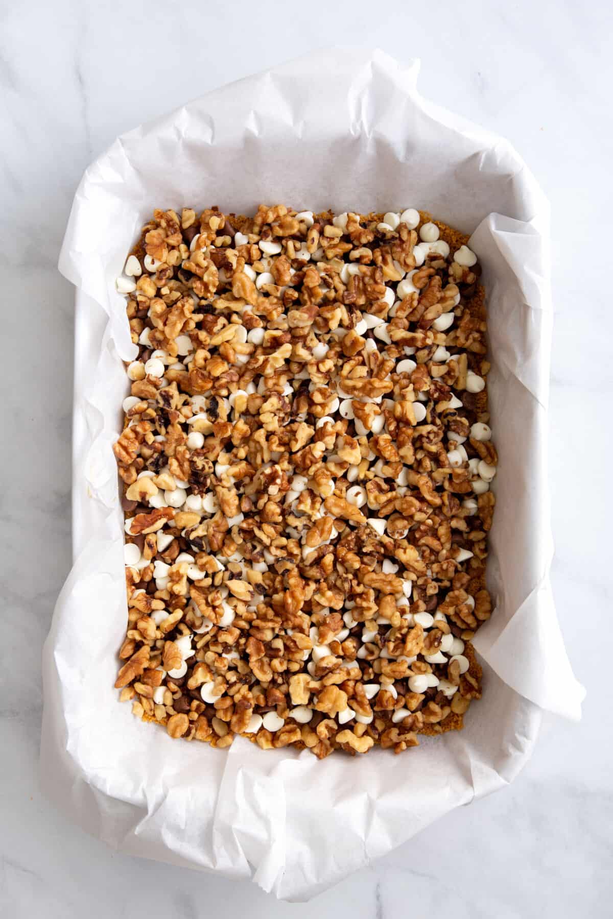 graham cracker crust pressed into a parchment paper lined 9x13 baking dish topped with a layer of milk and white chocolate chips, and chopped pecans