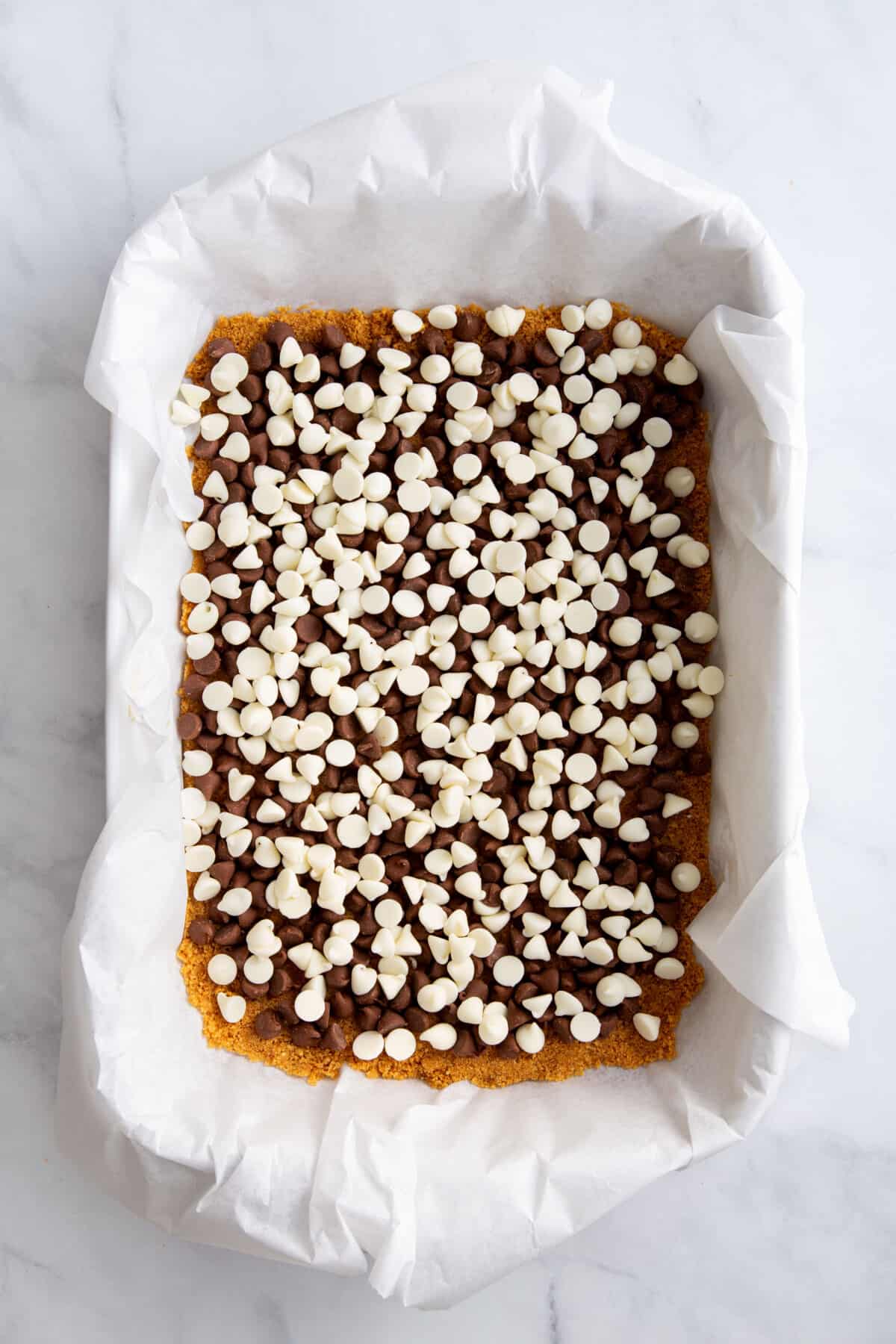 graham cracker crust pressed into a parchment paper lined 9x13 baking dish topped with a layer of milk and white chocolate chips