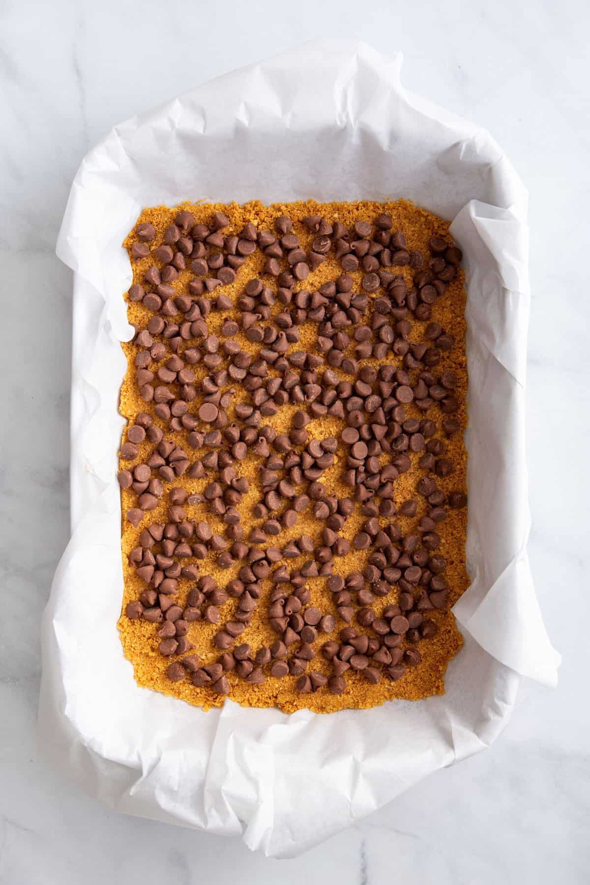 graham cracker crust pressed into a parchment paper lined 9x13 baking dish topped with a layer of milk chocolate chips