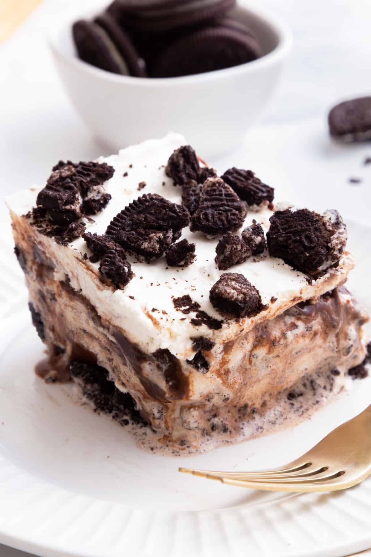 square slice of oreo ice cream cake served on a white round plate with a gold fork