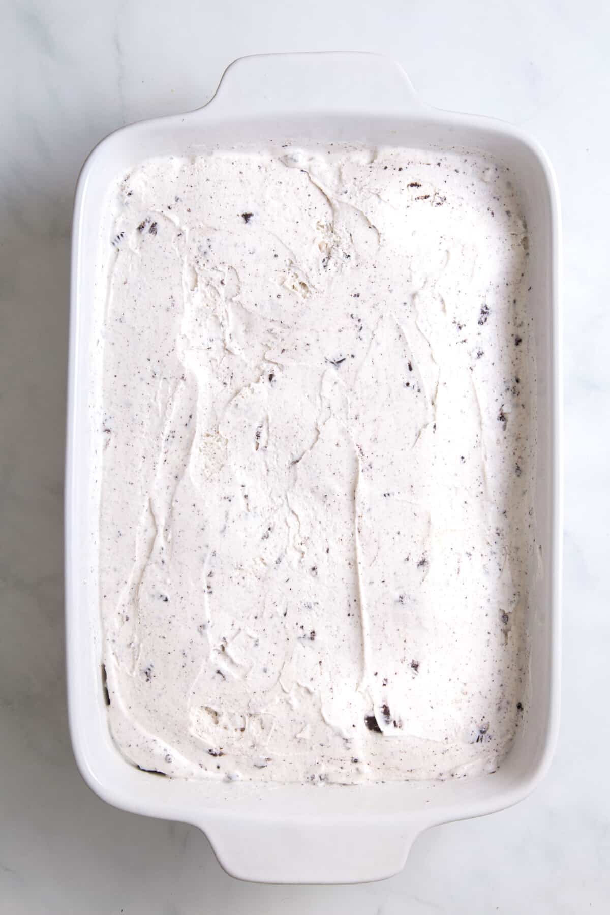 cookies and cream ice cream layered on top of crushed oreo crumbs sitting in a 9x13 casserole dish.