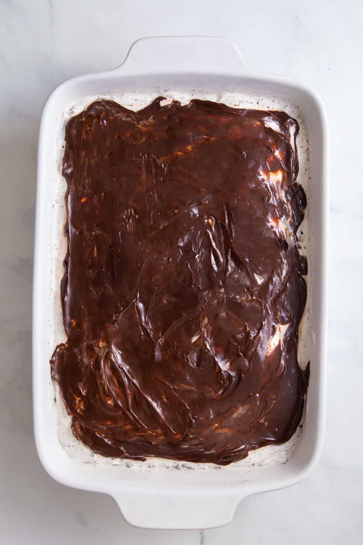 hot fudge layered on top of cookies and cream ice cream sitting in a 9x13 casserole dish.
