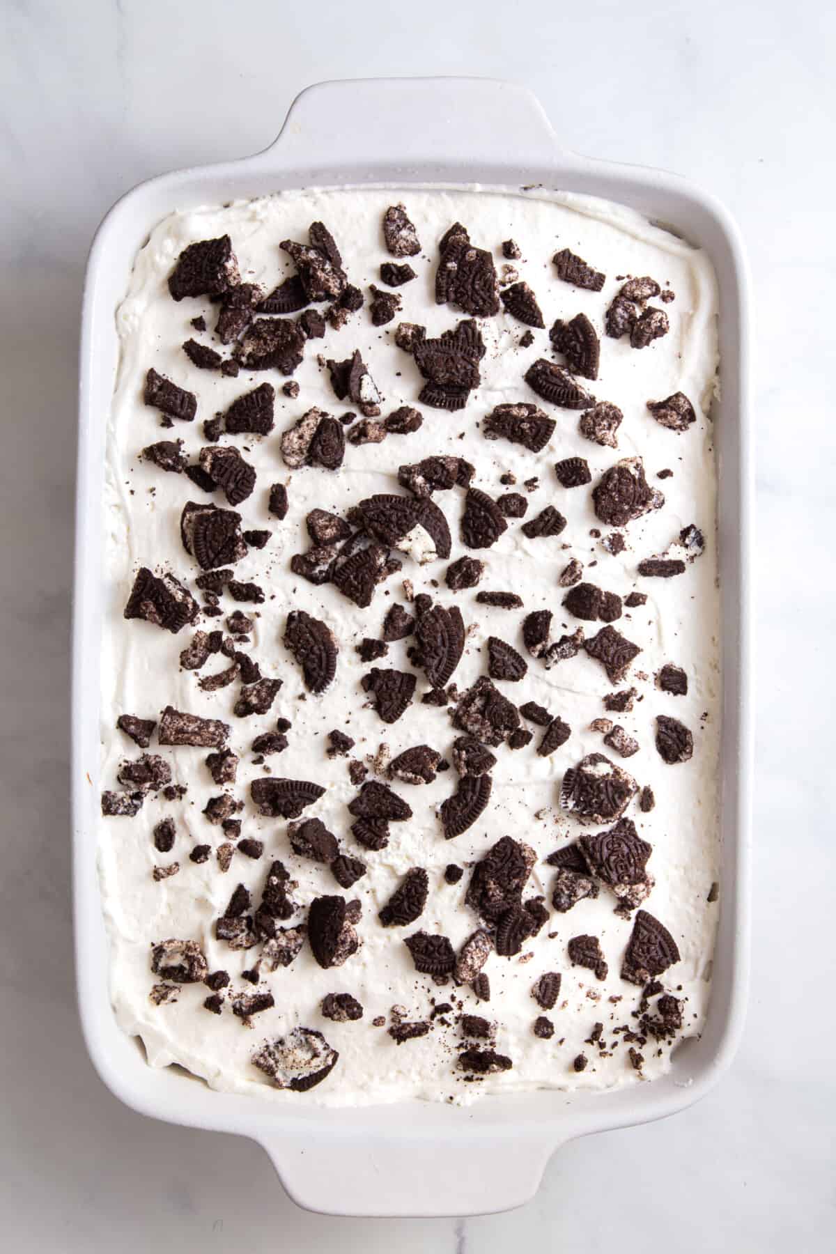 cool whip spread on top of oreo ice cream cake topped with extra crushed oreos sitting in a 9x13 casserole dish.