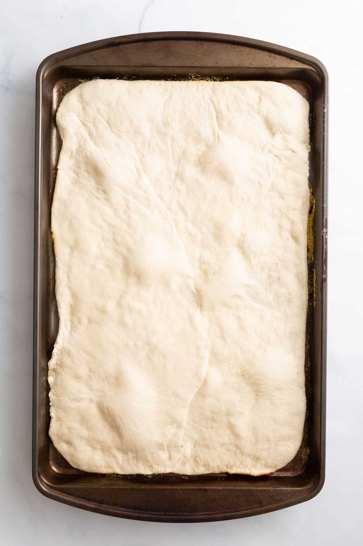 pizza dough layered at the bottom of a sheet pan