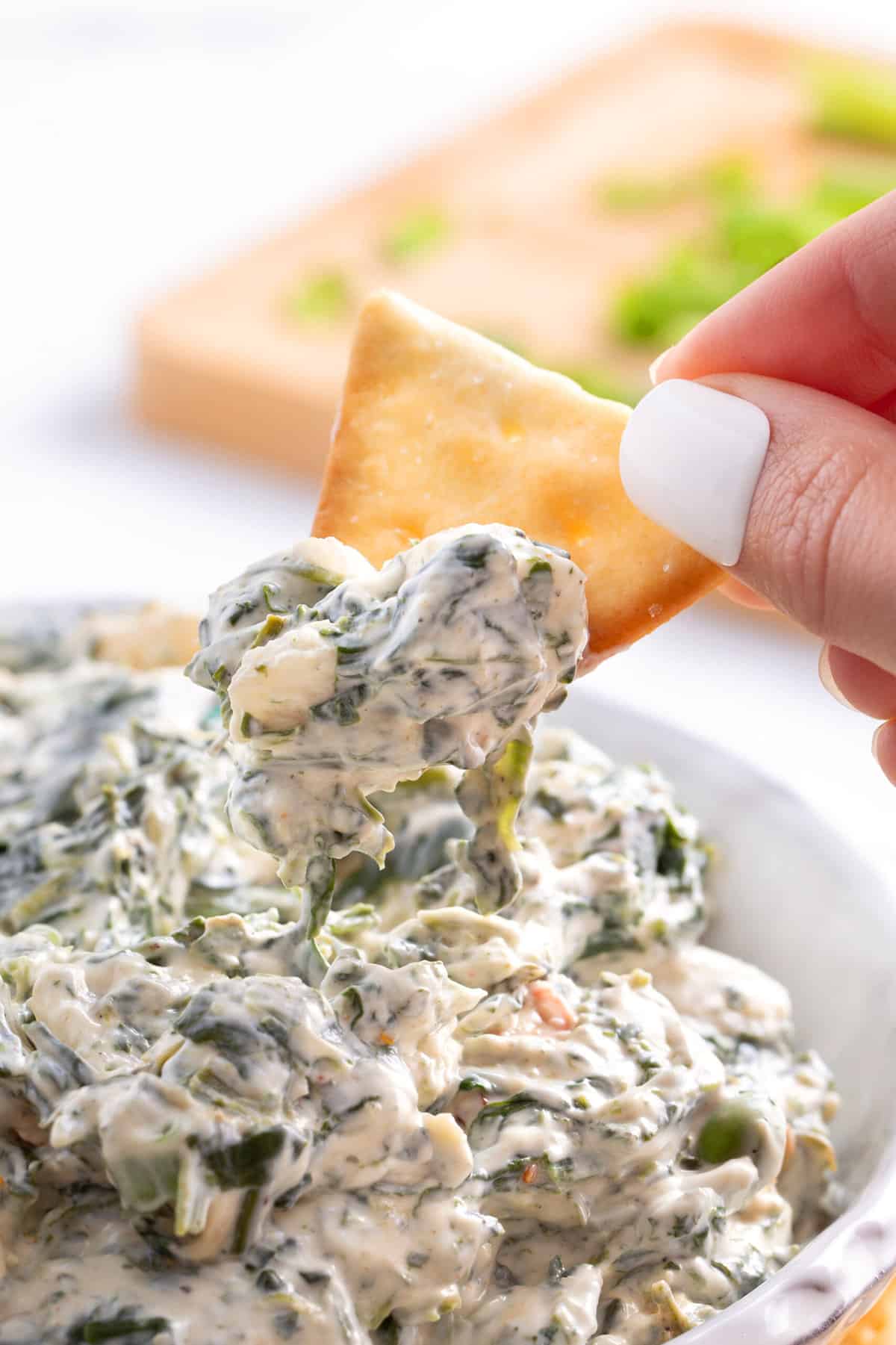 triangle shaped pita chip dipping into a bowl of spinach dip