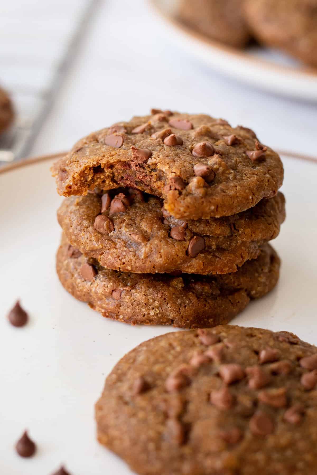 stack of three coffee cookies sitting on a plate with a bite taken out of the top cookie. 