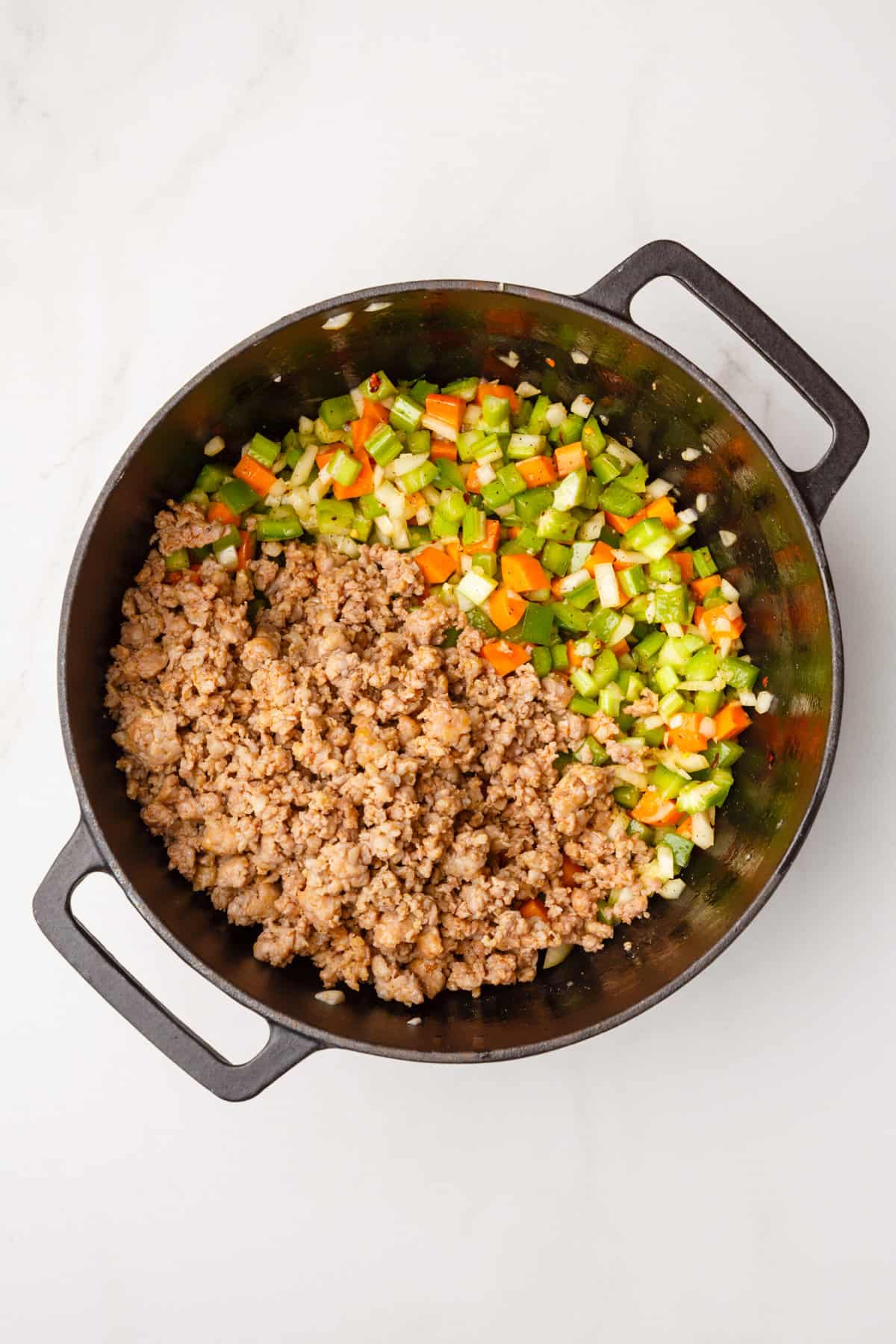 dutch oven with cooked chopped carrots, celery, green bell peppers, white onions and italian sausage