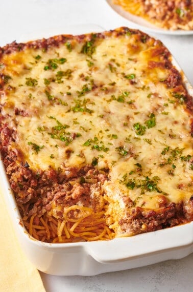 A baking dish of million dollar spaghetti with a large serving mixing.