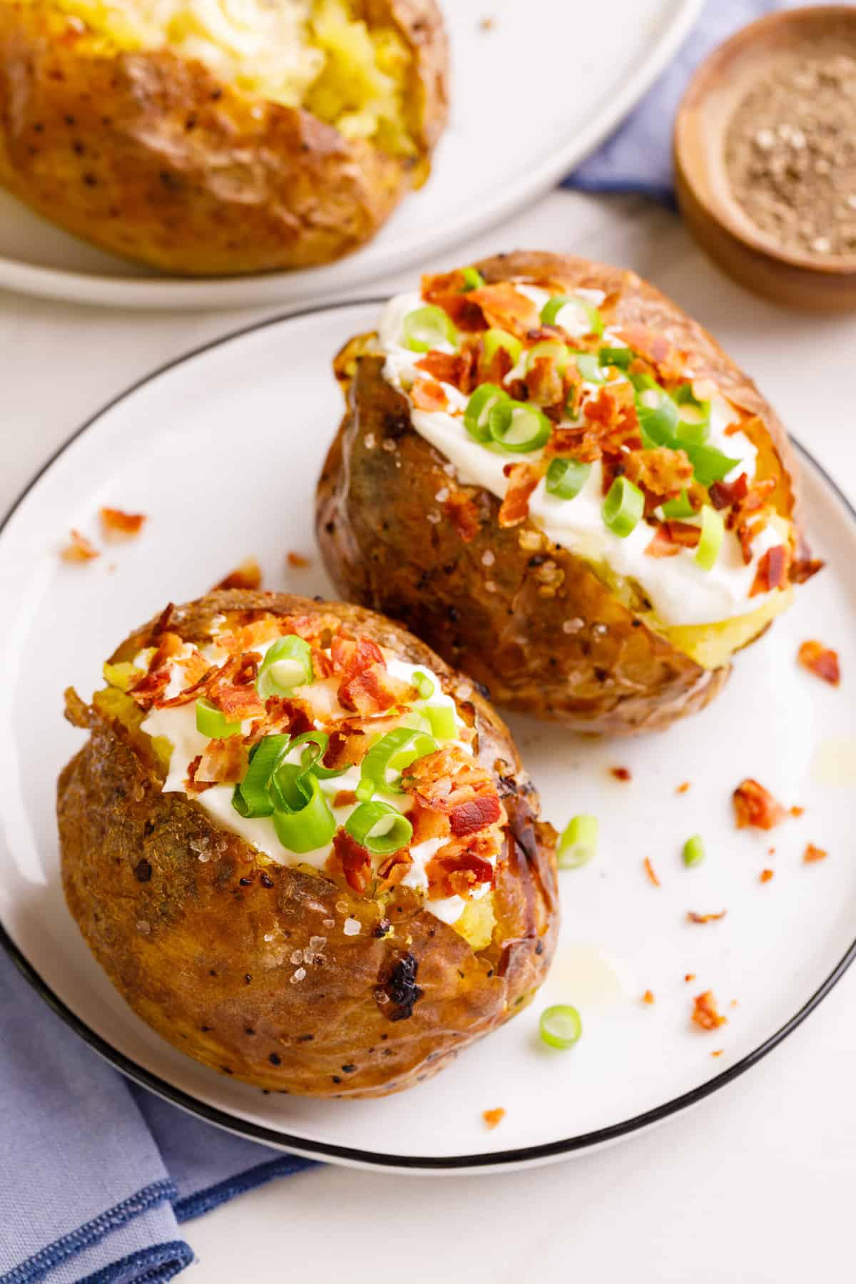 two loaded baked potatoes served on a white round plate