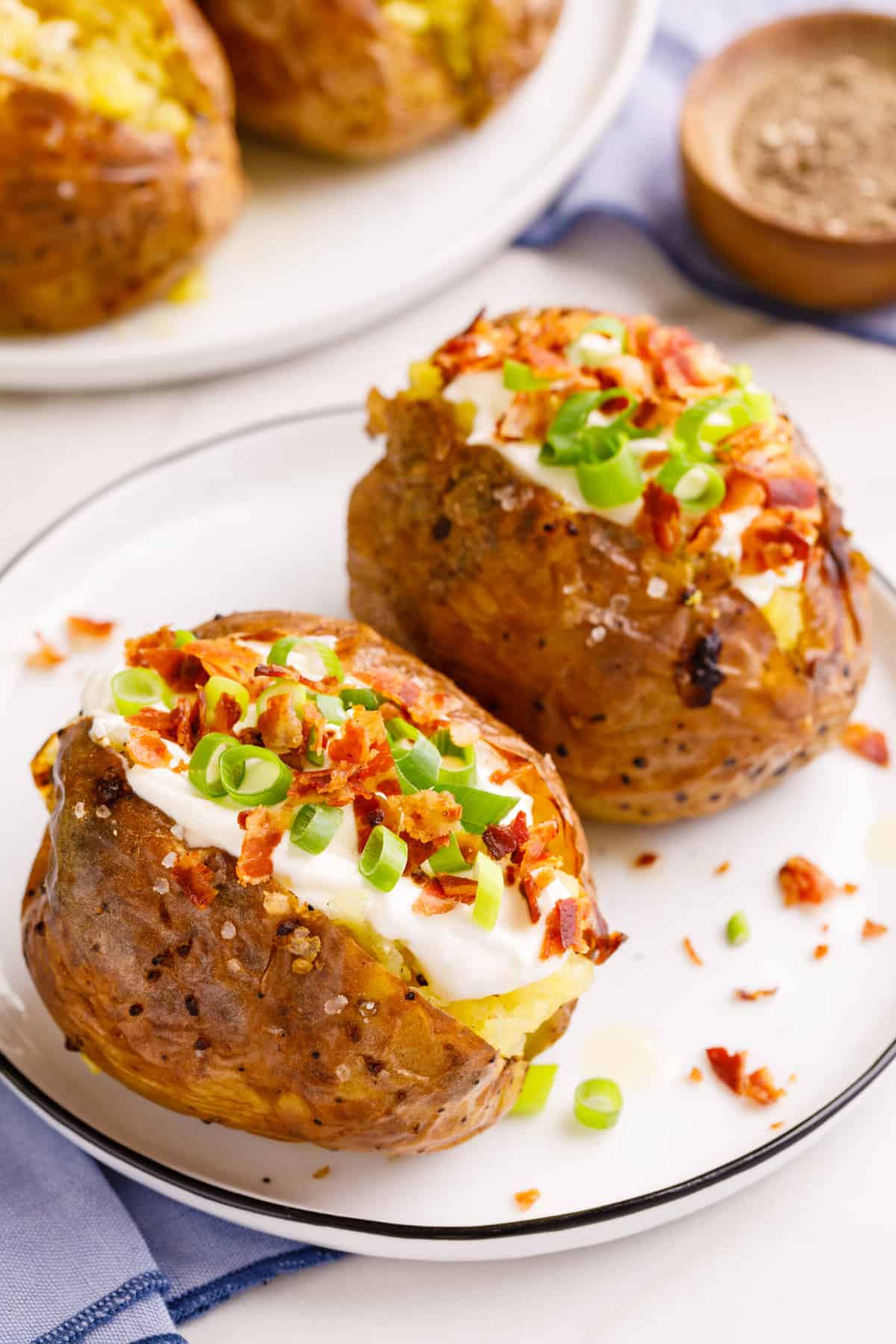 two loaded baked potatoes serve d on a white round plate.