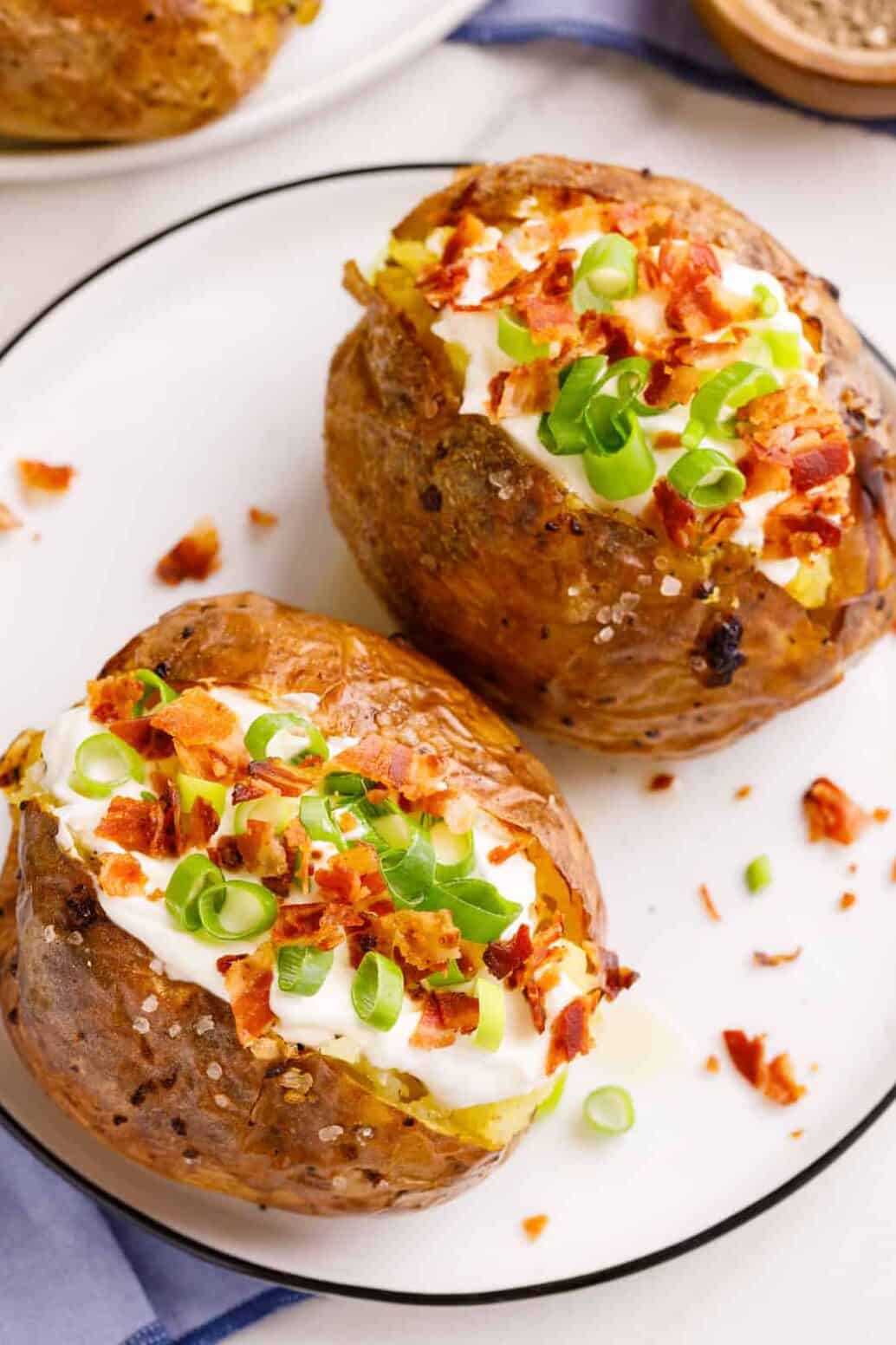 topo down image of two loaded baked potatoes served on a white round plate