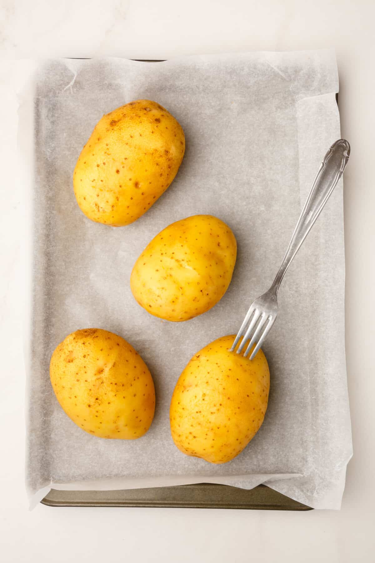 four russet potatoes sitting on a parchment-lined baking sheet.