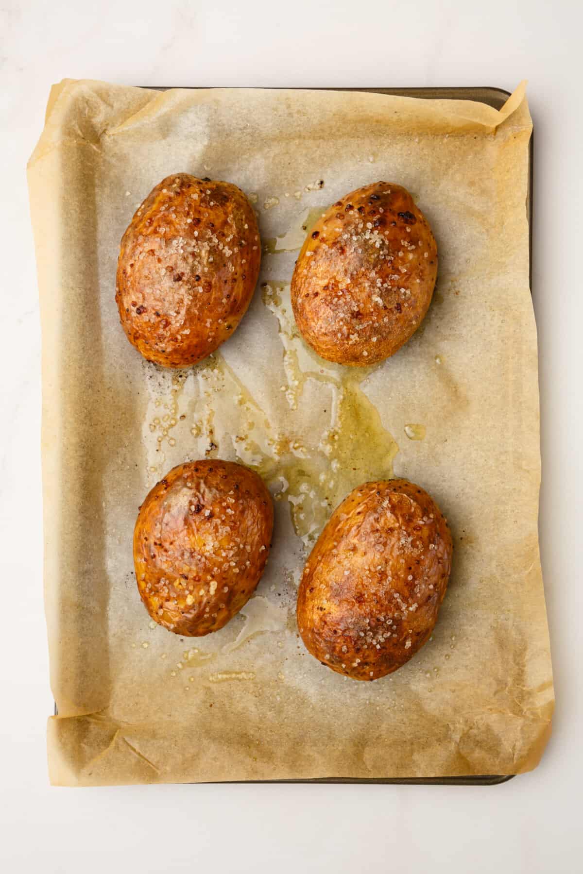 four baked russet potatoes sitting on a parchment lined baking sheet.