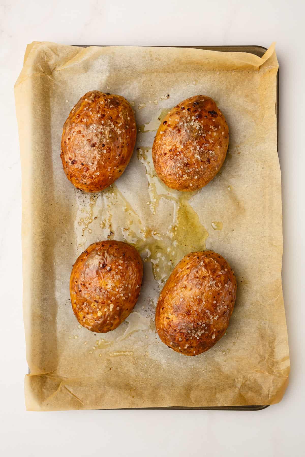 four baked russet potatoes sitting on a parchment lined baking sheet