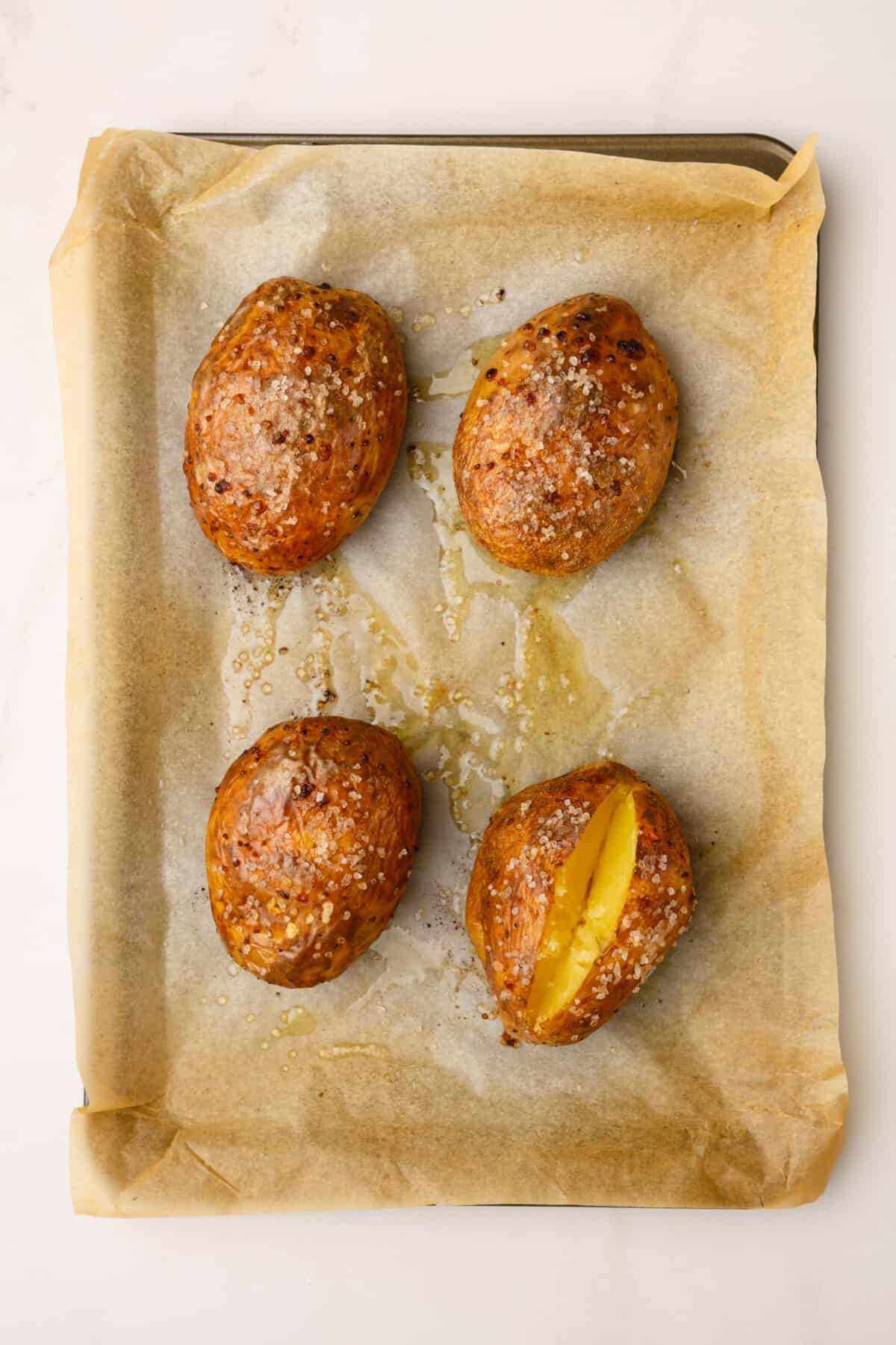 four baked russet potatoes sitting on a parchment lined baking sheet.