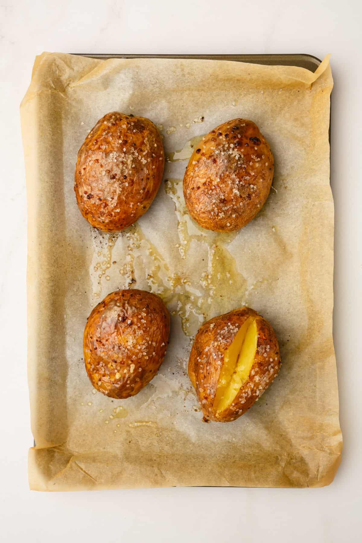 four baked russet potatoes sitting on a parchment lined baking sheet