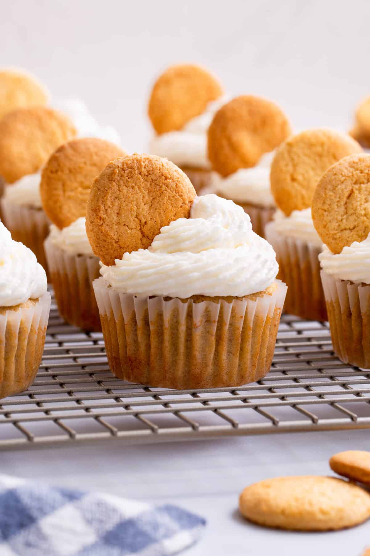 Banana pudding cupcakes topped with a Nilla wafer on a wire rack.