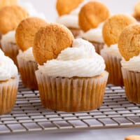 Banana pudding cupcakes topped with a Nilla wafer on a wire rack.