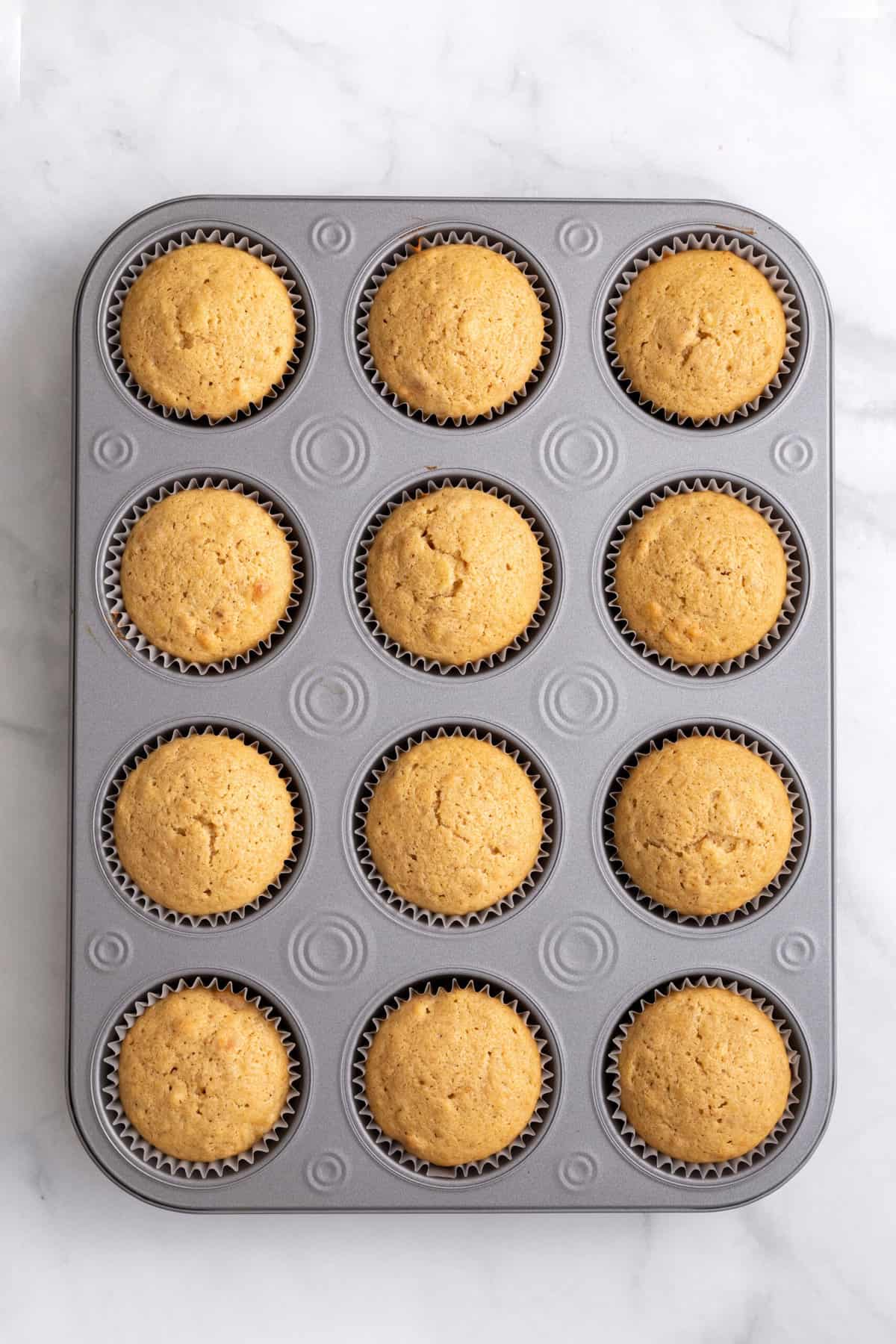 12 baked banana pudding cupcakes sitting in a muffin tin.