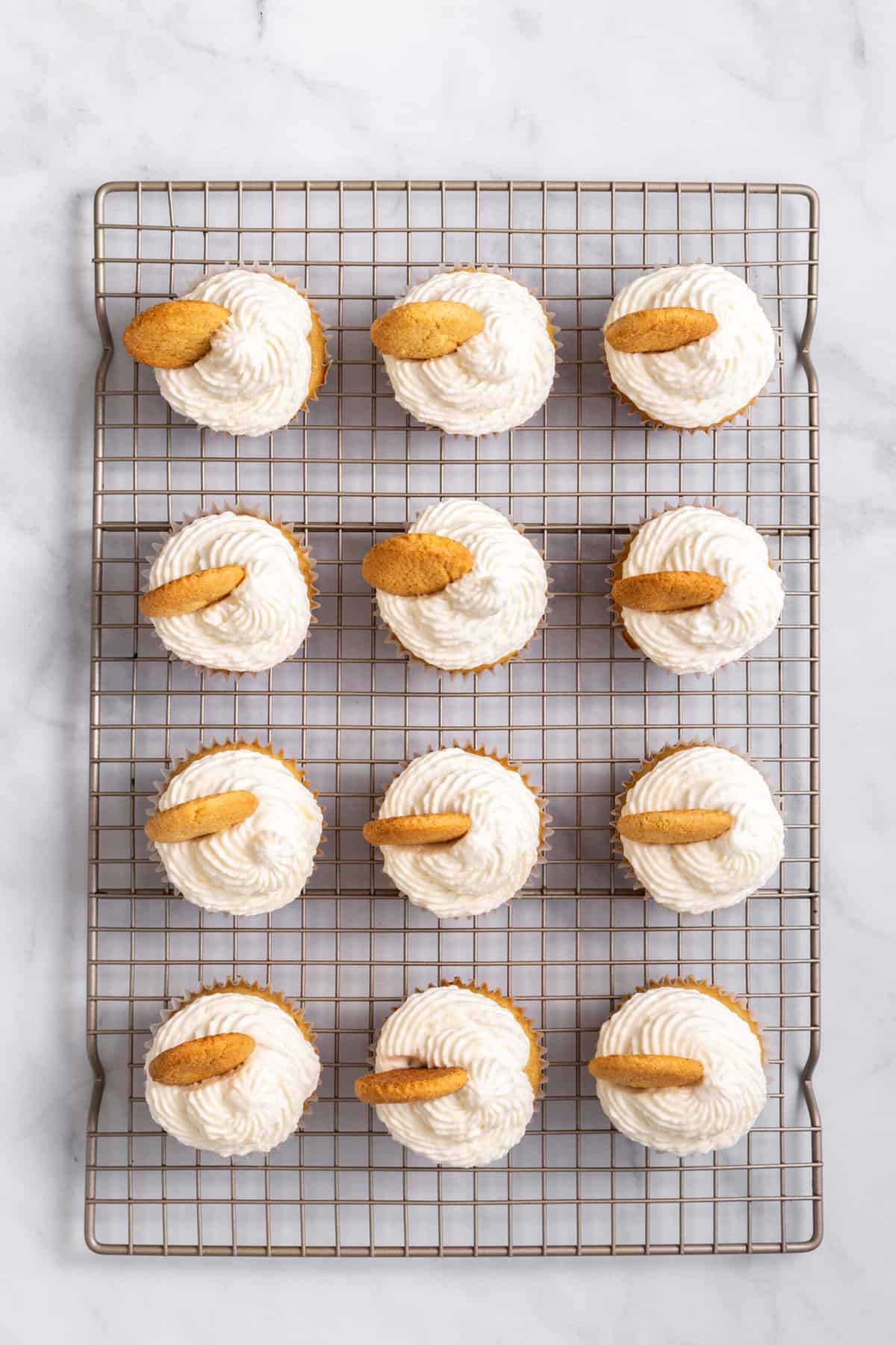 12 prepared banana pudding cupcakes sitting on a cooling rack.