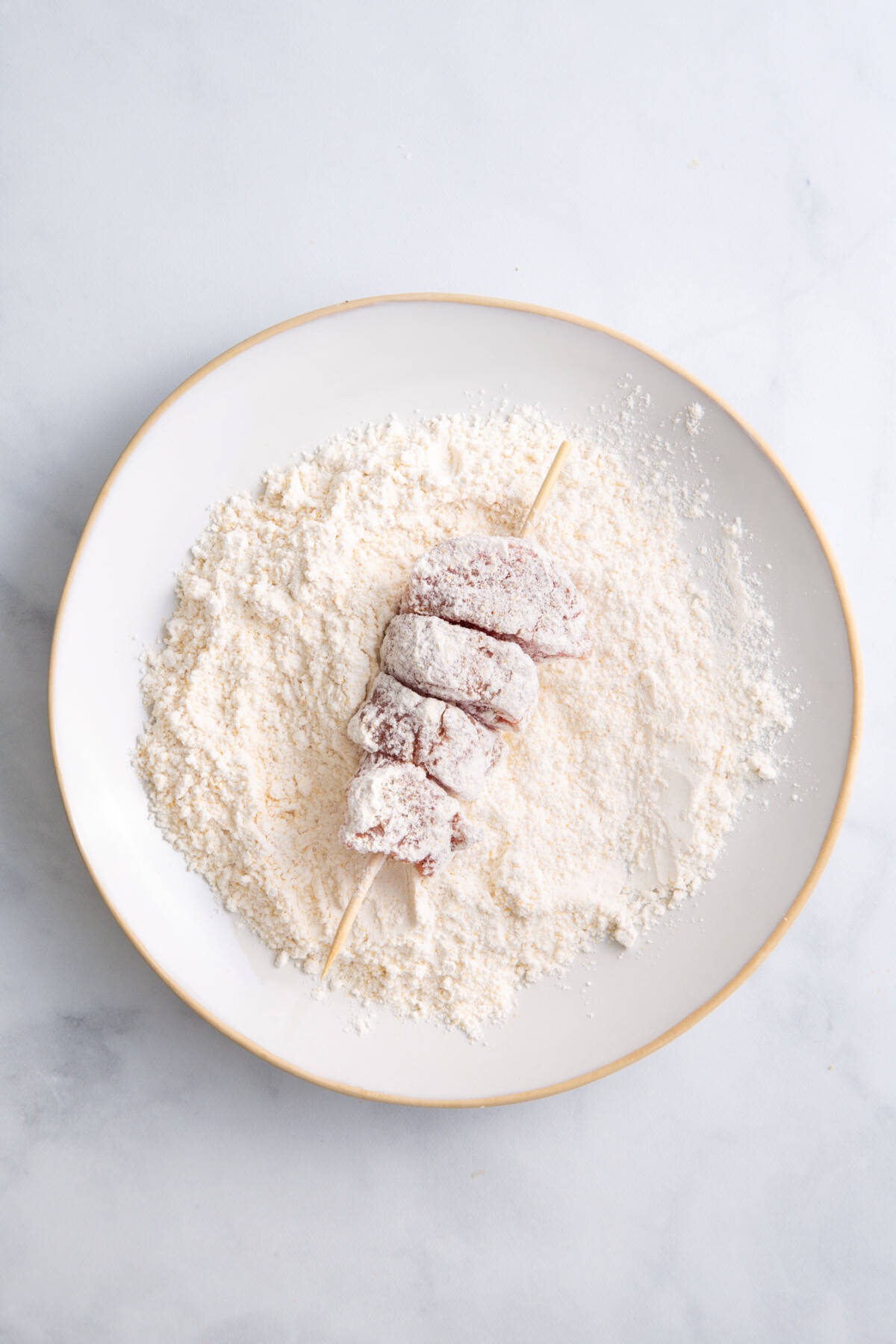 Pork skewers being dredged in flour.