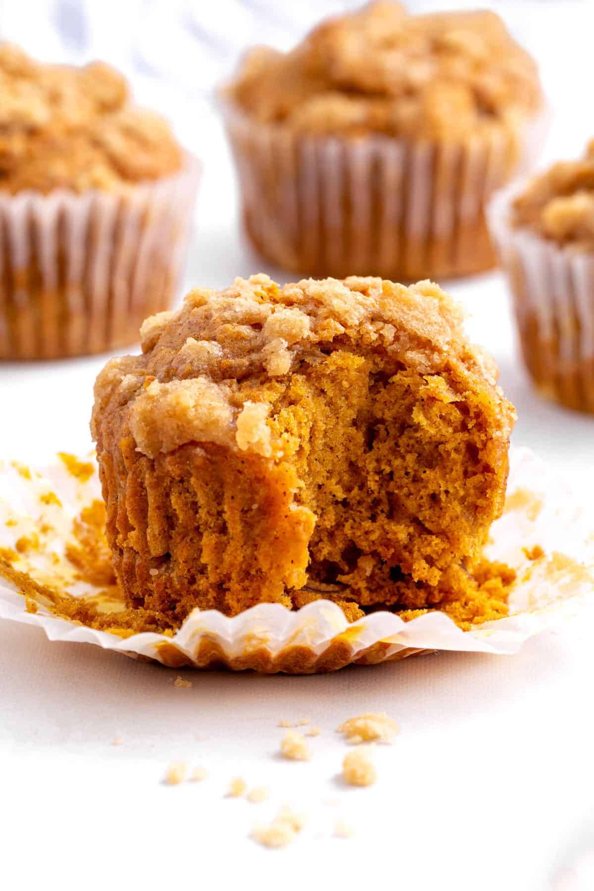 close up image of a pumpkin apple muffin with the liner taken off and a bite taken into it