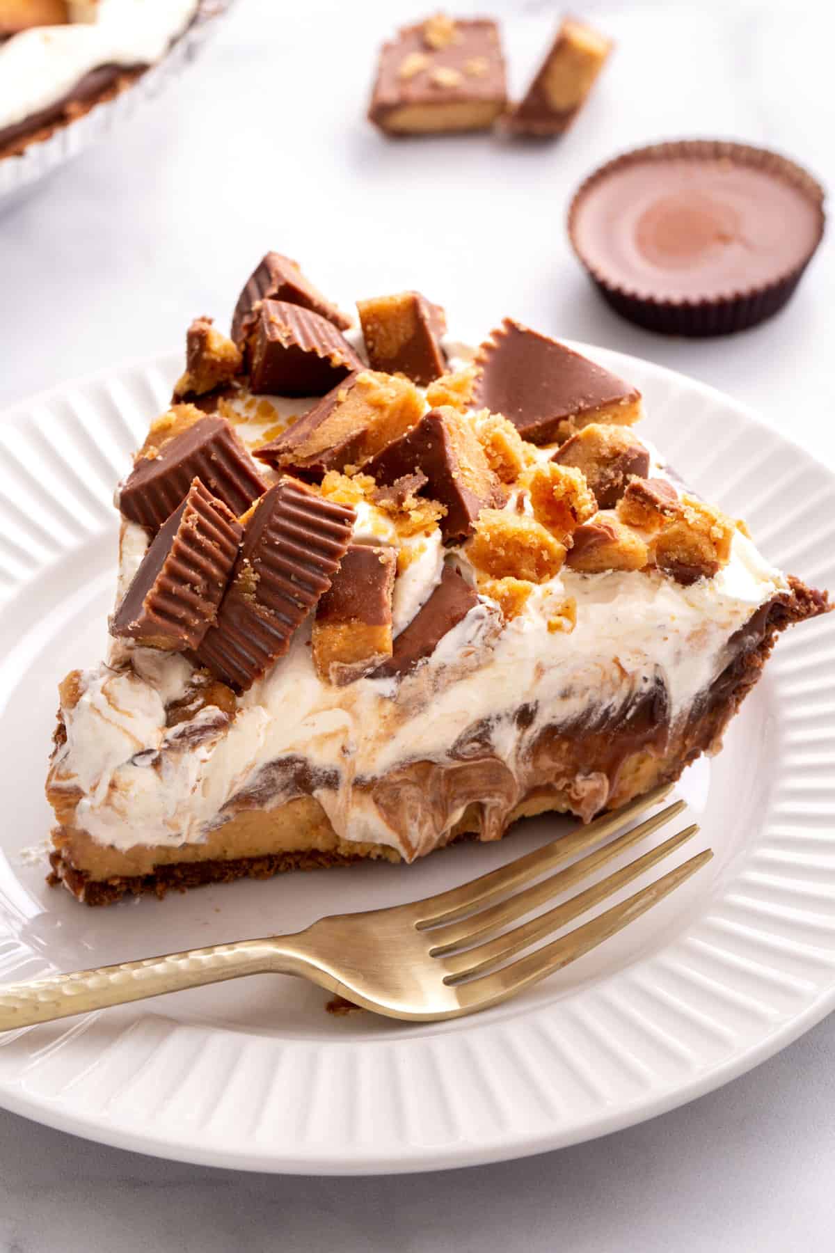 slice of reese's peanut butter pie sitting on a white round plate with a gold fork.