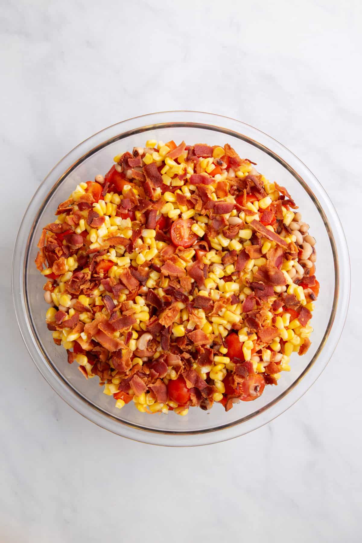 large glass bowl of black-eyed peas, halved cherry tomatoes, crumbled bacon and sweet corn kernels.