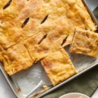A tray of apple slab pie with pieces being lifted up.