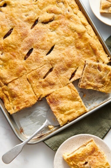 A tray of apple slab pie with pieces being lifted up.