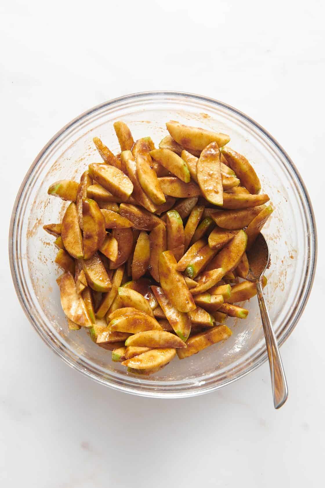 large glass bowl of sliced green apples tossed in a cinnamon, brown sugar mixture.
