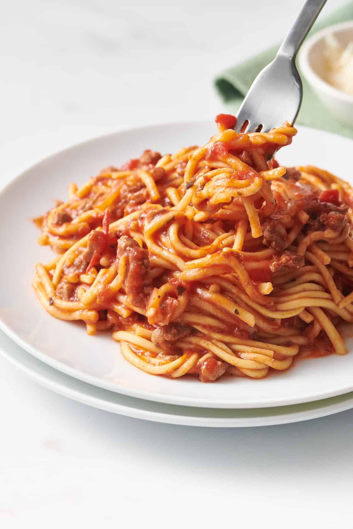 forkful of crock pot spaghetti served on a stack of two white round plate. 