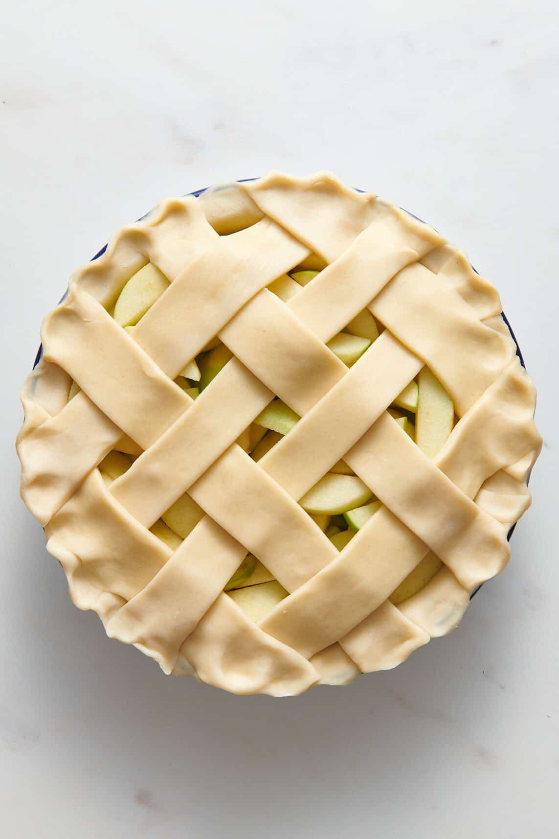 pie crust lined pan with sliced granny smith apples topped with a lattice pattern made of pie crust.