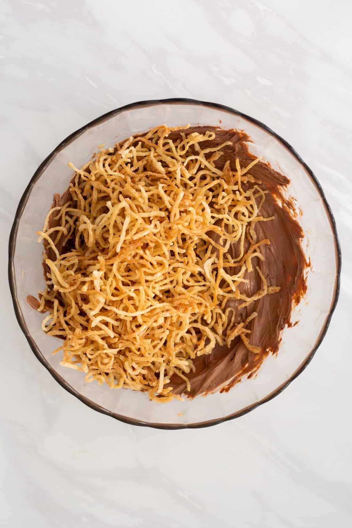melted butterscotch chips, chocolate chips, peanut butter, vanilla extract and crispy chow mein noodles sitting in a large glass bowl. 