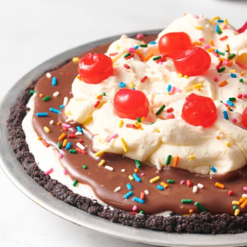 An Oreo crust ice cream pie topped with whipped cream and cherries.