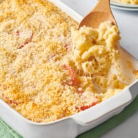 A wooden spoon lifting a scoop of Ina Garten mac and cheese from a baking dish.