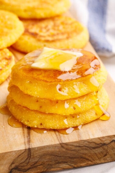 A stack of cornbread fritters topped with butter and honey.
