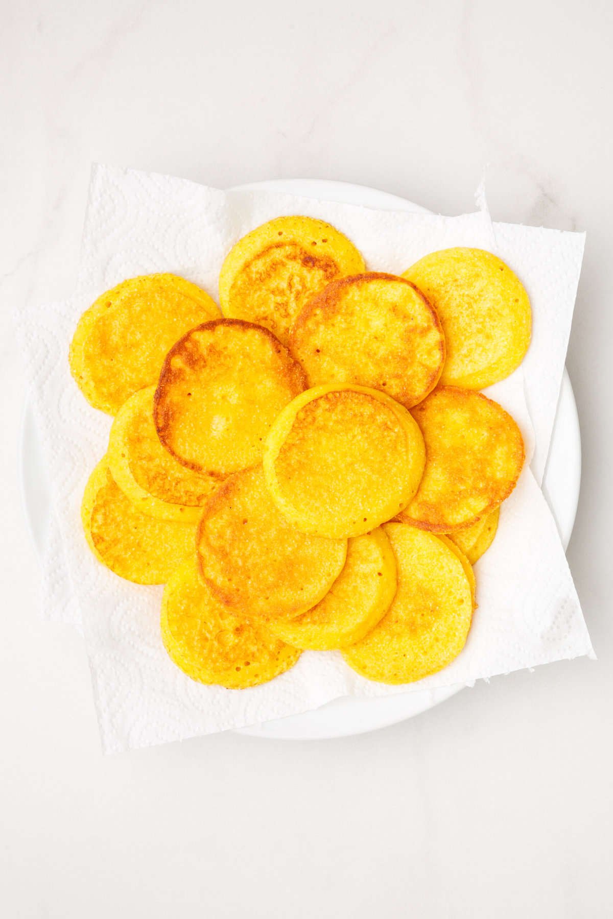 a pile of fried cornbread fritters sitting on a paper towel-lined plate. 