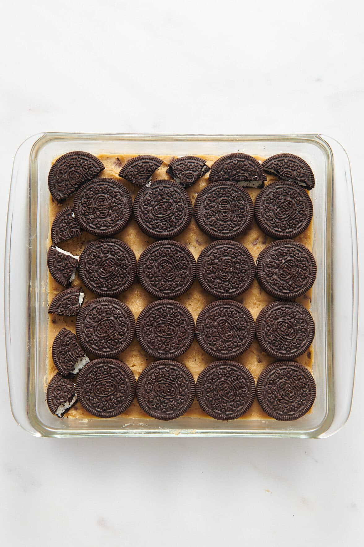 chocolate chip cookie dough batter layered at the bottom of a 9x9 glass baking dish and layered with Oreo cookies on top.
