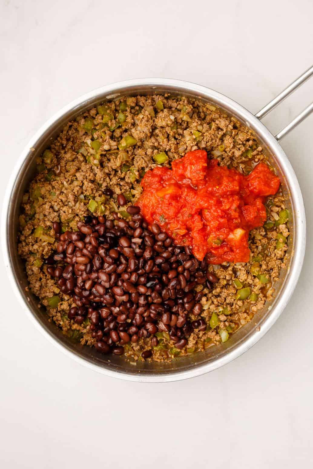 cooked ground beef, onion, green bell peppers, black beans and rotel tomatoes in a stainless steel pan.