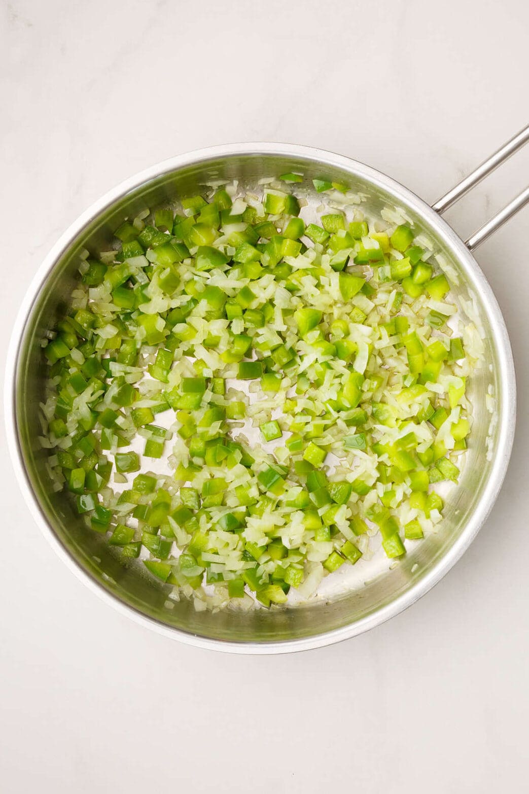 chopped onion and green bell peppers sitting in a stainless steel pan. 